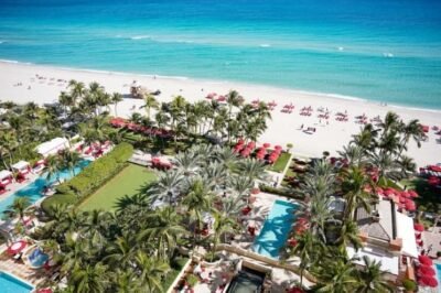 Luxo na praia com vista para o oceano azul, área de resort com piscinas, espreguiçadeiras e redes sob palmeiras, perfeito para férias relaxantes e experiências inesquecíveis no SuoViaggio.