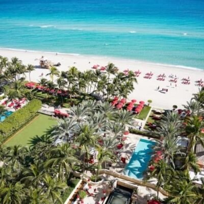 Luxo na praia com vista para o oceano azul, área de resort com piscinas, espreguiçadeiras e redes sob palmeiras, perfeito para férias relaxantes e experiências inesquecíveis no SuoViaggio.