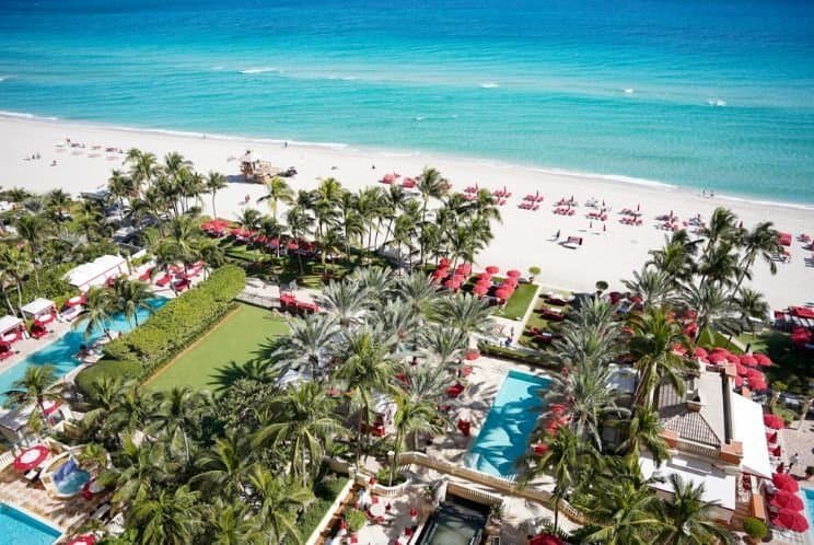 Luxo na praia com vista para o oceano azul, área de resort com piscinas, espreguiçadeiras e redes sob palmeiras, perfeito para férias relaxantes e experiências inesquecíveis no SuoViaggio.