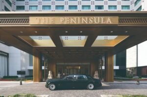 Lindo hotel de luxo The Peninsula com entrada imponente, decoração elegante e carro clássico na frente, ideal para viagens de negócios ou lazer na cidade.