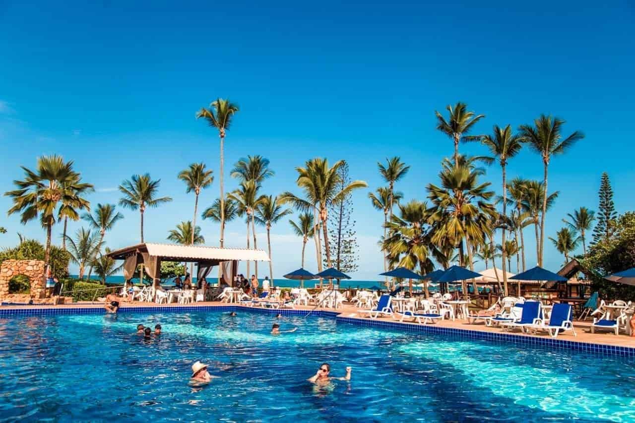 Relaxamento na piscina de resort paradisíaco com palmeiras, espreguiçadeiras e sombra para férias tropicais perfeitas em destinos de luxo.