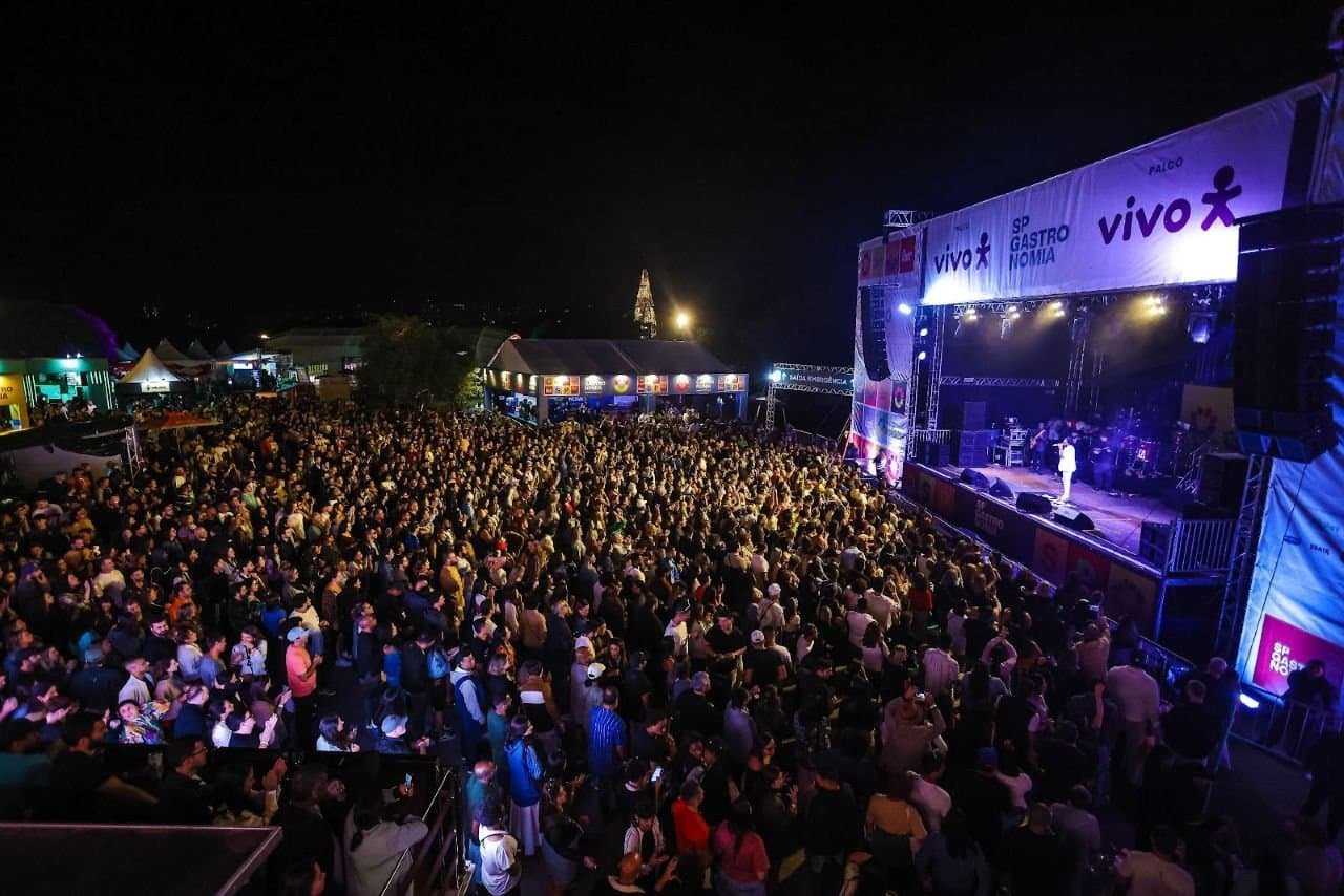 Festival de música ao vivo com grande público durante evento cultural em São Paulo, com palco iluminado, artistas performando e multidão aproveitando a noite de entretenimento e gastronomia no espaço público.