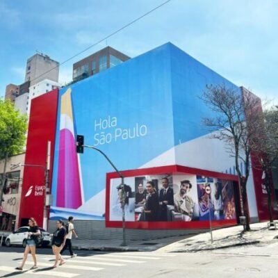 - Fachada de prédio em São Paulo com grande banner azul e mensagens acolhedoras para turistas e visitantes.