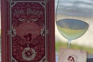 Luz de vinho branco ao lado do livro de Jane Austen sobre romance clássico, com vista para o mar ao fundo, ideal para viagens de lazer, leitura e apreciação de vinhos em destinos turísticos no Brasil e mundo.