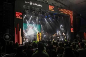 Público assistindo a show no evento de turismo Expo Rio Rio Janeiro, com palco iluminado, banda performing e destaque para o cenário de feira de turismo da cidade.