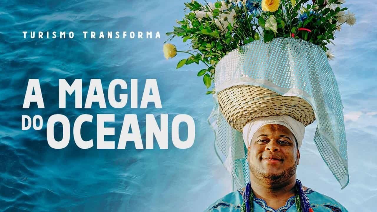 Imagem de um homem com um chapéu decorado com flores e uma cesta de palha na cabeça, simbolizando a conexão com o oceano e o turismo sustentável.